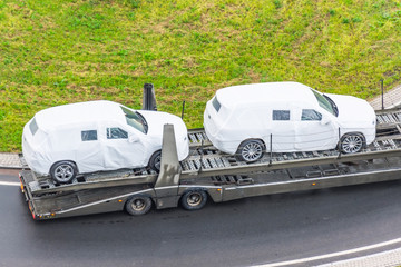 Transportation of new cars covered with protective fabric tarp on a truck trailer.