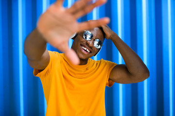 Young black man with sunglasses standing against blue background, black lives matter concept.