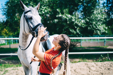 Young woman petting muzzle of white horse