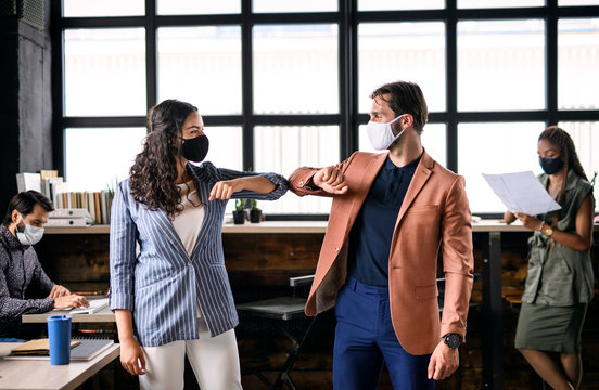 Young businesspeople with face masks working indoors in office, greeting.