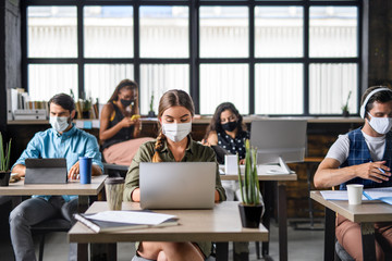 Portrait of young businesspeople with face masks working indoors in office.