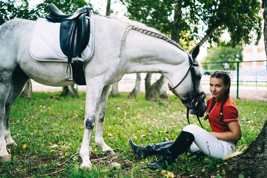 Glad Female Jockey Stroking Horse On Green Lawn