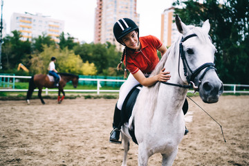 Female equestrian in black helmet caressing horse in paddock