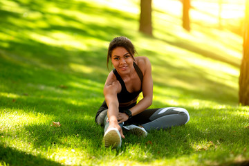Happy black sporty girl stretching muscles, exercising at park