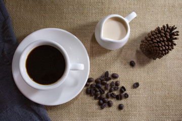 a coffee cup beside milk jar place on hemp sack and beside a pin