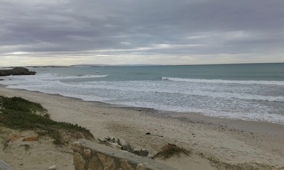 The beautiful backdrop of the sea, sandy shores scattered with rocks layered into the skies of grey in South Africa