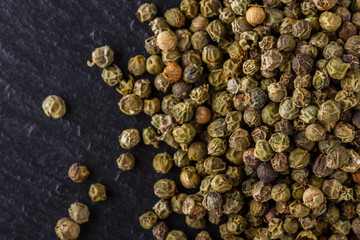 green peppercorns on dark slate stone background