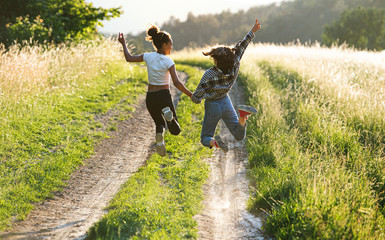 Rear view of young teenager girls friends outdoors in nature, jumping.