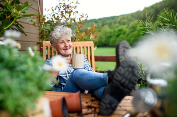 Senior woman with coffee sitting on terrace in summer, resting.