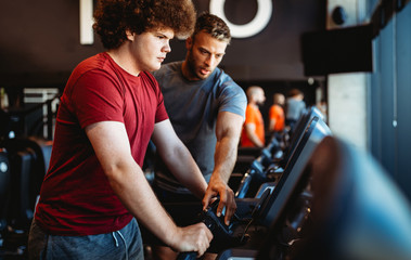 Overweight young man exercising gym with personal trainer