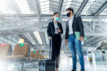 two asian business partners with face mask protection social distancing new normal lifestyle Business travellers walking in airport with luggage