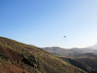 Paraglider flying over the Teide National Park and silhouette of the Astronomical Observatory of...