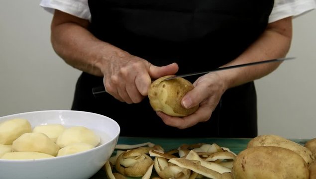 Las manos de una mujer quitan la piel de las patatas con el cuchillo

