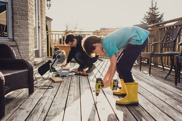 Father and son working on fixing a deck with power tools together.