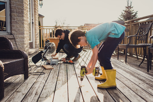 Father And Son Working On Fixing A Deck With Power Tools Together.