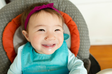 Adorable smiling baby girl wearing headband sits in highchair at home