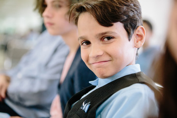 Boy sitting and dressed in vest and button up smiles at the camera