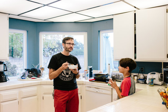 Father and son in a kitchen having a chat while dad eats cereal