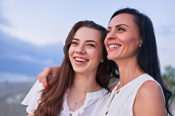 Happy attractive smiling daughter hugging with laughing mother and having fun together outdoors