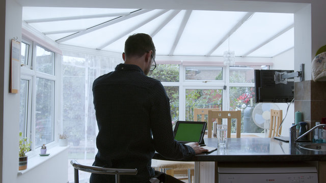 Male professional using a green screen tablet while working from home in a kitchen