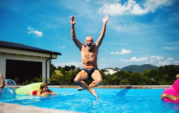 Group of cheerful seniors in swimming pool outdoors in backyard, jumping.