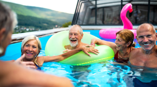 Group of cheerful seniors in swimming pool outdoors in backyard, talking.