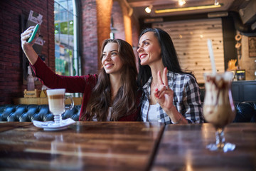 Casual happy smiling joyful mother and daughter taking a selfie photo on a phone camera and having good time together in a coffee shop
