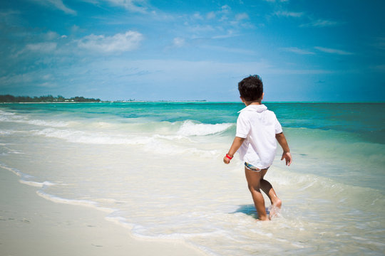 Little boy walking at the beach watching Caribbean ocean
