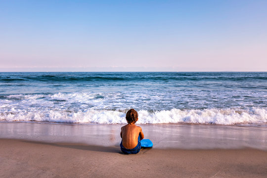 rear view of 5 years old kid sitting at the beach facing the ocean