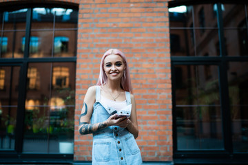 Half length portrait of cheerful female blogger with tattooed hand smiling at camera during leisure...