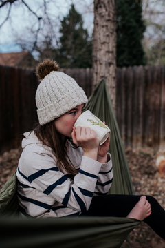 Teen girl sitting in hammock drinking from mug