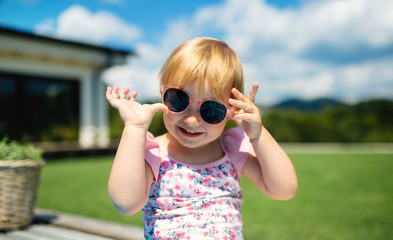 Portrait of small toddler girl with sunglasses outdoors in backyard garden.