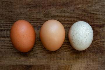 Three multi-colored chicken eggs on a natural wooden background. Close-up, top view.