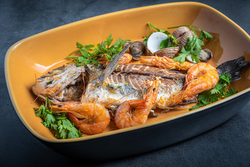 Sea bream cooked with prawns and parsley in an orange baking dish.