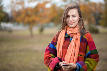 young woman in autumn park listening to music enjoying good weather wearing warm woolen clothes