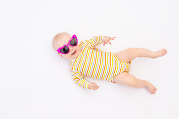 small smiling baby girl 6 months old lying on a white isolated background in bright sunglasses, space for text
