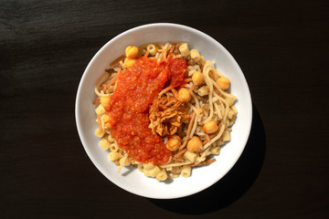 Famous traditional Arabic, Egyptian dish - Koshari. National Kushari in a white plate on dark wooden background. Flat lay, top view.