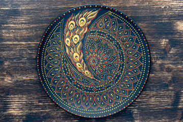 Decorative ceramic plate with black, red and golden colors, painted plate on wooden background , dot painting