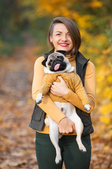 Naklejka na ściany i meble Girl holding her pug dog in the autumn in the park