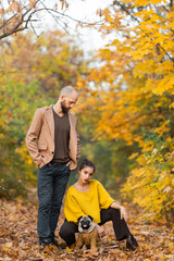 bearded man and girl with pug in autumn in maple park