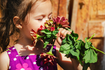 Obraz na płótnie Canvas The child breathes in the scent of summer flowers. A bouquet of flowers in children's hands close-up. Portrait photo of a kid with flowers. Happy child portrait photo. Baby face with flowers close up.