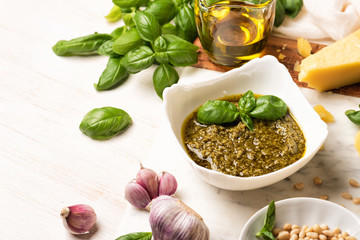 Bowl with pesto and fresh basil, garlic, parmesan cheese, pine nuts and olive oil on marble board. Kitchen wooden table with Italian sauce