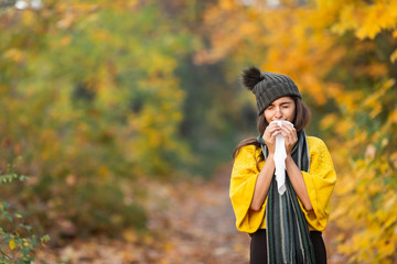 girl sneezes into a headscarf in autumn in the park. allergy or viral infection concept
