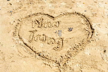Two footprints of pebble feet on the surface of the sea sand of the desert and the word Nha Trang and the heart is drawn in the sand. Games on the sand and on the beach. A copy of the space