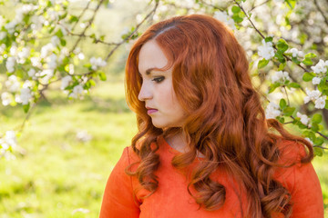 Naklejka premium Portrait of a red-haired girl walking in an apple orchard in an orange dress