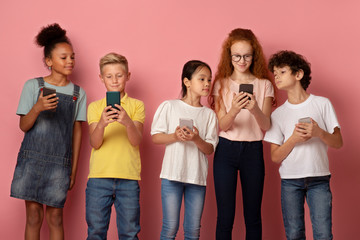 Modern technologies in schooling. Multiethnic kids using cellphones together over pink background