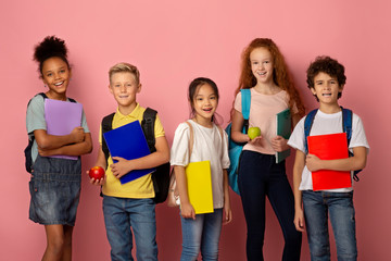 Getting ready for new school year. Diverse children with backpacks, notebooks and apple fruits on pink background