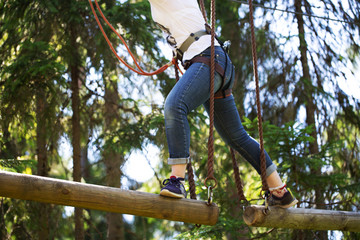 A young woman in equipment overcomes an obstacle in a rope Park