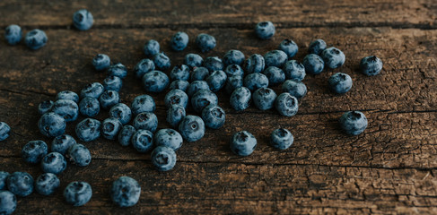 Blue fresh blueberries are scattered on an old brown wooden cracked table.