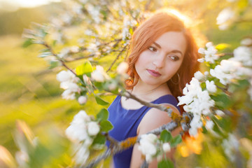Tiltshift Portrait of a red-haired girl walking in an apple orchard in an blue dress